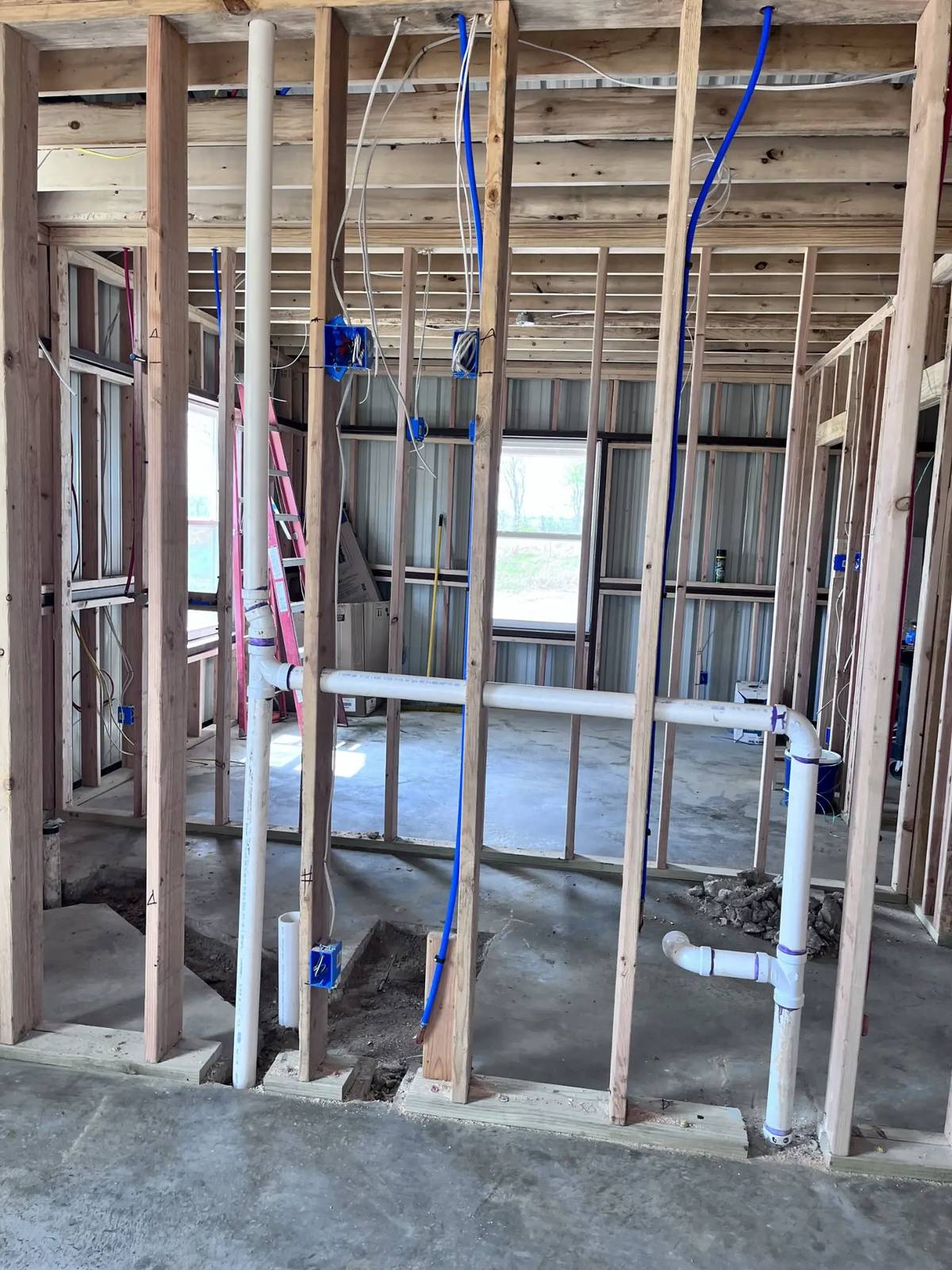 Framed walls with PVC drains, vents, and PEX water lines in a metal building