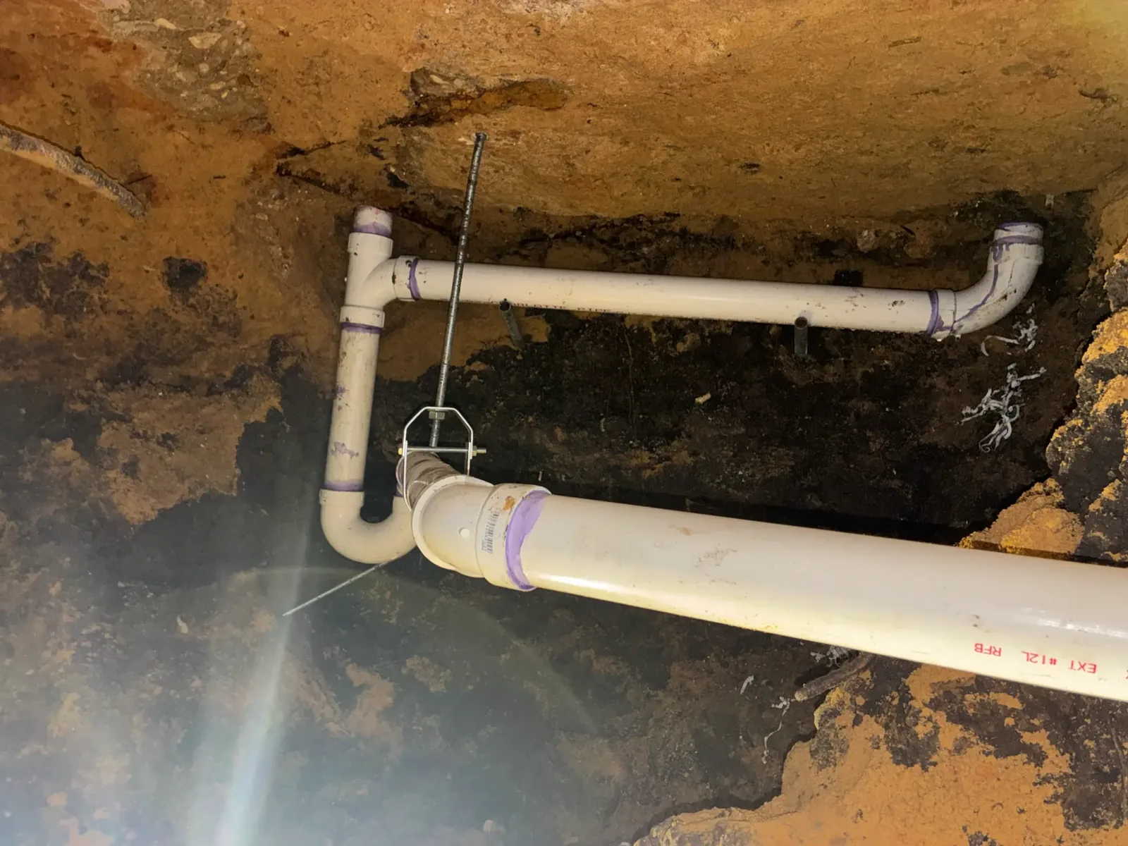 White drain piping and fittings visible in an open under-slab excavation
